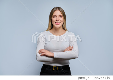 Smiling young woman with arms crossed in studio against grey background 143743719