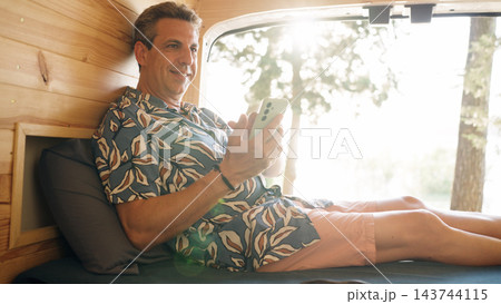 Mature man relaxing, using smartphone in camper van 143744115