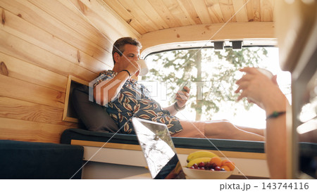 Mature couple enjoying coffee and phone in camper van 143744116