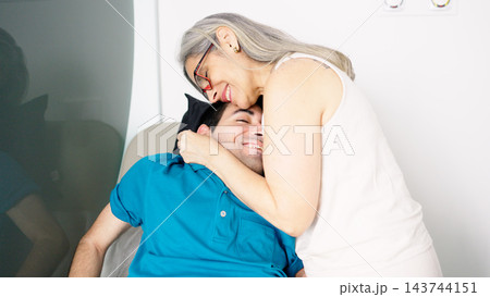 Mother embracing adult son with physical disability in hospital Mother embracing adult son with physical disability in hospital 143744151