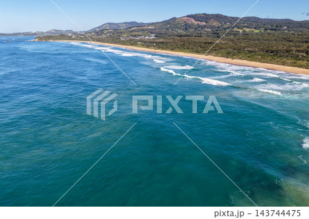 Aerial view of waves breaking along Sapphire Beach near Coffs Harbour, with turquoise ocean, a long sandy shoreline and forested coastal hills. Aerial view of waves breaking along Sapphire Beach near Coffs Harbour, with turquoise ocean, a long sandy shoreline and forested coastal hills. 143744475