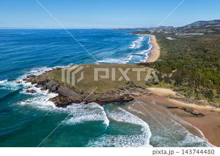 Aerial view of Green Bluff View Point, a grassy headland overlooking a sandy beach and surf along the Coffs Harbour coast, New South Wales, Australia. Aerial view of Green Bluff View Point, a grassy headland overlooking a sandy beach and surf along the Coffs Harbour coast, New South Wales, Australia. 143744480