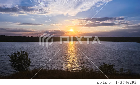 Golden sunset reflecting on a rippling lake beneath dramatic clouds Golden sunset reflecting on a rippling lake beneath dramatic clouds 143746293