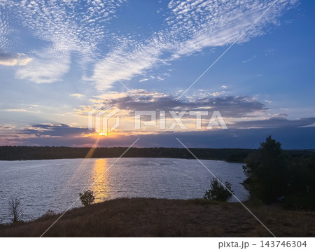 Sunset over a lake beneath a textured blue sky 143746304