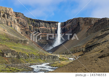 Hengifoss waterfall and red layered basalt cliffs above a rocky river in East Iceland Hengifoss waterfall and red layered basalt cliffs above a rocky river in East Iceland 143746553