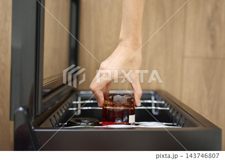 Hand places glass drink bottle inside cooler with other bottles and cans 143746807