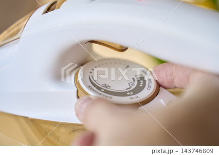Closeup of person turning temperature control dial on electric iron 143746809