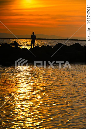 夕日に照らされた海岸と人物のシルエット(新潟県新潟市) 夕日に照らされた海岸と人物のシルエット(新潟県新潟市) 143747014