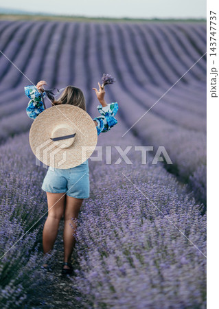 Lavender field woman Young woman with straw hat and floral top standing in blooming purple lavender rows for summer travel Lavender field woman Young woman with straw hat and floral top standing in blooming purple lavender rows for summer travel 143747737