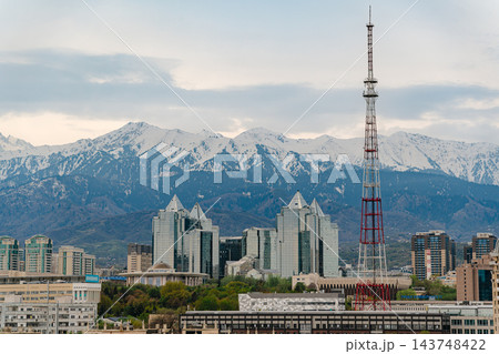 Almaty city skyline with snow capped mountains, red and white TV tower and green spring trees 143748422