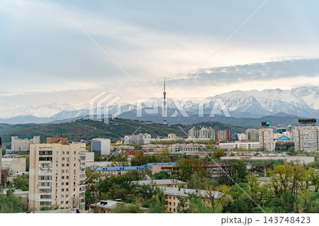 Almaty city skyline with snow capped mountains, red and white TV tower and green spring trees 143748423