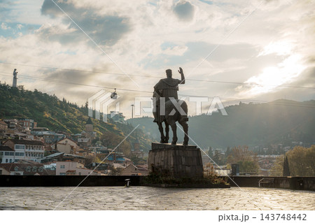 Sunburst behind equestrian statue on a cobblestone terrace with Tbilisi old town and cable car Sunburst behind equestrian statue on a cobblestone terrace with Tbilisi old town and cable car 143748442