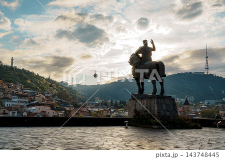 Sunburst behind equestrian statue on a cobblestone terrace with Tbilisi old town and cable car Sunburst behind equestrian statue on a cobblestone terrace with Tbilisi old town and cable car 143748445