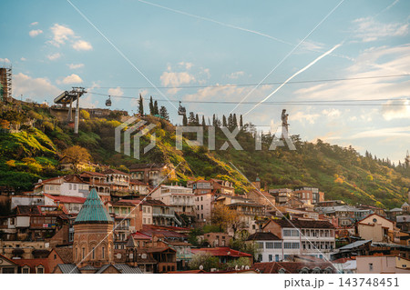 Cable car cabins over old town houses with Mother of Georgia statue on the hill at sunset in Tbilisi Cable car cabins over old town houses with Mother of Georgia statue on the hill at sunset in Tbilisi 143748451