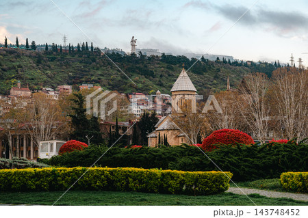 Conical dome church among park hedges with red shrubs and Mother of Georgia statue on a hill in Tbilisi Conical dome church among park hedges with red shrubs and Mother of Georgia statue on a hill in Tbilisi 143748452