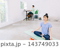 リビングでヨガをする妻とその奥で仕事をする夫 143749033
