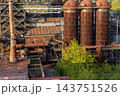 High angle telephoto landscape of historic blast furnace cowper stoves with dome tops white bridge gas pipelines rusty metal roofing and green tree canopy in Duisburg Ruhr region Germany 143751526