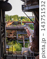 Vertical photo of historic blast furnace pipe bridge with rusty steel gas pipelines catwalk walkways support girders and green forest canopy in Duisburg North Landscape Park Ruhr region Germany 143751532