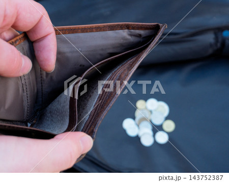 Hands holding open an empty brown leather wallet. Poverty and financial crisis concept with blurred coins in background Hands holding open an empty brown leather wallet. Poverty and financial crisis concept with blurred coins in background 143752387