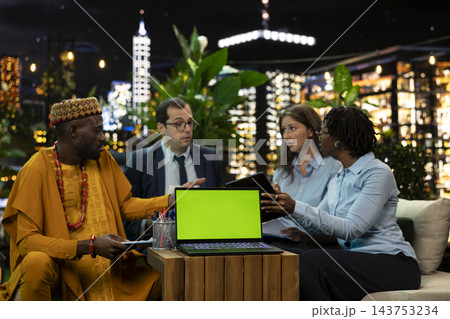 Green screen, laptop and business team as colleagues discuss paperwork behind blank chroma display on table. Screen replacement, collaboration and planning support mockup in rooftop lounge at night. 143753234