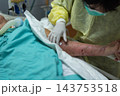 A healthcare worker wearing gloves face mask protective gown leans over patient arm during bedside care green bedding equipment visible the hospital room background 143753518