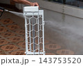 A person holds white air conditioner filter frame upright while spraying it water wet tiled floor mesh panel geometric protective grid visible the cleaning view 143753520