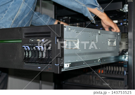 A technician denim sleeve works metal server unit extended from an equipment rack drive bays orange release tabs cables visible close view of hardware maintenance 143753525
