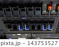 Rows of black server drive bays blue release handles fill equipment rack indicator lights upper hardware panels visible close view of computer data storage equipment 143753527