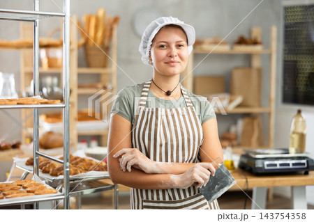 Young baker girl is standing near work table in kitchen, working with dough 143754358