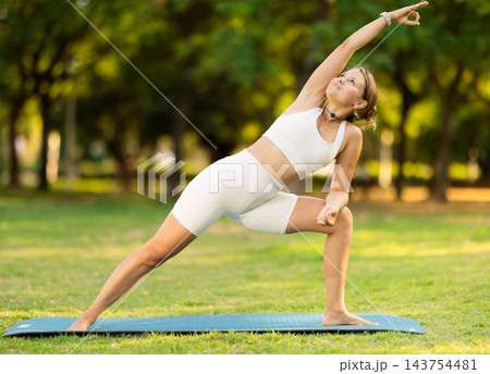 Girl performing Extended Side Angle Pose during yoga practice outdoors 143754481