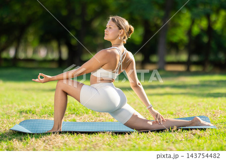 Girl in park on green grass of lawn performs Anjaneyasana 143754482