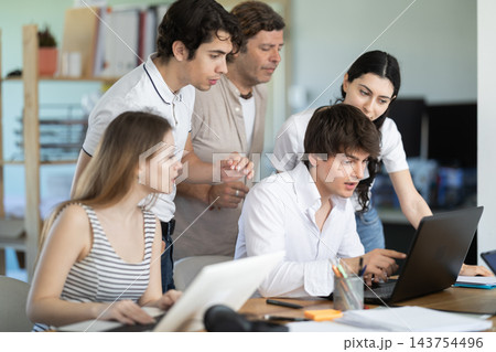 Colleagues looking at one laptop together in office Colleagues looking at one laptop together in office 143754496