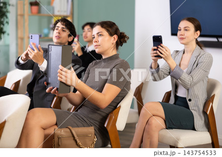 Focused group of students sitting on chairs and listening lecture, taking photo or QR with mobil or tablet in lecture hall Focused group of students sitting on chairs and listening lecture, taking photo or QR with mobil or tablet in lecture hall 143754533