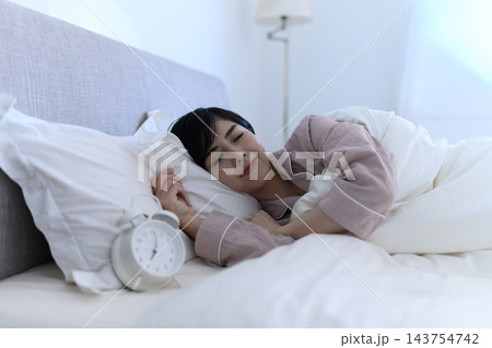 目覚まし時計が鳴る朝にベッドで眠る女性 143754742