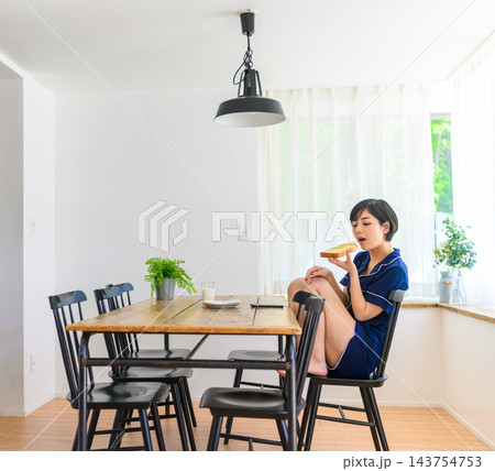 食卓でトーストを食べるパジャマ姿の女性 143754753