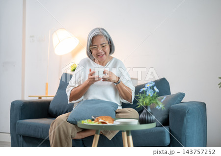 Senior Asian woman smiling while holding coffee cup on living room sofa. 143757252