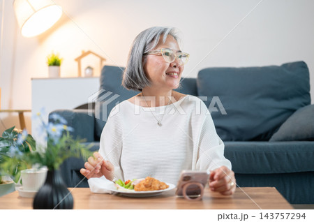 Senior Asian Woman Enjoy Eating Morning Breakfast with Smartphone 143757294