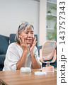 Elderly asian woman massaging face with moisturizing cream. 143757343