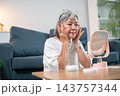 Mature woman doing facial lifting massage looking in mirror. 143757344