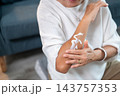Close up of a senior woman's hand applying white body lotion cream on her arm. 143757353