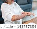 Close up of a mature asian woman smoothing moisturizing lotion over forearm. 143757354