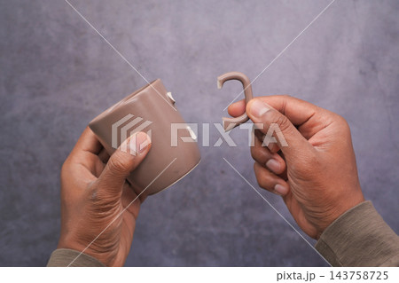 Hands hold a broken brown mug and its detached handle 143758725