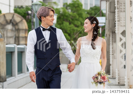 都会の橋の上を手をつないで歩く新郎新婦 143759431
