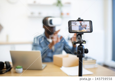 A creator tests immersive technology at a home workspace, with a phone recording the demonstration beside a laptop, shipping boxes, and paper notes A creator tests immersive technology at a home workspace, with a phone recording the demonstration beside a laptop, shipping boxes, and paper notes 143759558