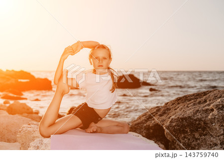 Flexible child practicing advanced yoga pose on rocky seashore during warm sunset light Flexible child practicing advanced yoga pose on rocky seashore during warm sunset light 143759740