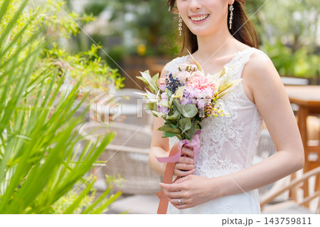 屋外のオープンなテラスでブーケを持ち微笑むウェディングドレス姿の花嫁 屋外のオープンなテラスでブーケを持ち微笑むウェディングドレス姿の花嫁 143759811