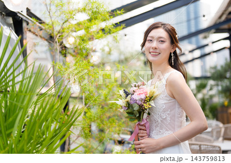 屋外のオープンなテラスでブーケを持ち微笑むウェディングドレス姿の花嫁 屋外のオープンなテラスでブーケを持ち微笑むウェディングドレス姿の花嫁 143759813