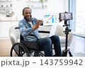 A smiling professional presents a rising chart to a phone camera from his wheelchair in a bright home office, sharing business results with viewers online 143759942