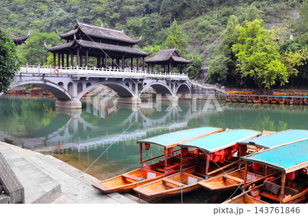 Fenghuang Ancient Town - tourist attraction in Hunan, China. Traditional chinese boats and old bridge in watertown Fenghuang - City of Phoenix. Summer topic of travel, trip, vacation Fenghuang Ancient Town - tourist attraction in Hunan, China. Traditional chinese boats and old bridge in watertown Fenghuang - City of Phoenix. Summer topic of travel, trip, vacation 143761846