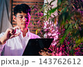 Marijuana researcher Asian man wearing glasses and holding a vial bottle and a clipboard to check list in cannabis sativa hemp plants in cannabis farms 143762612